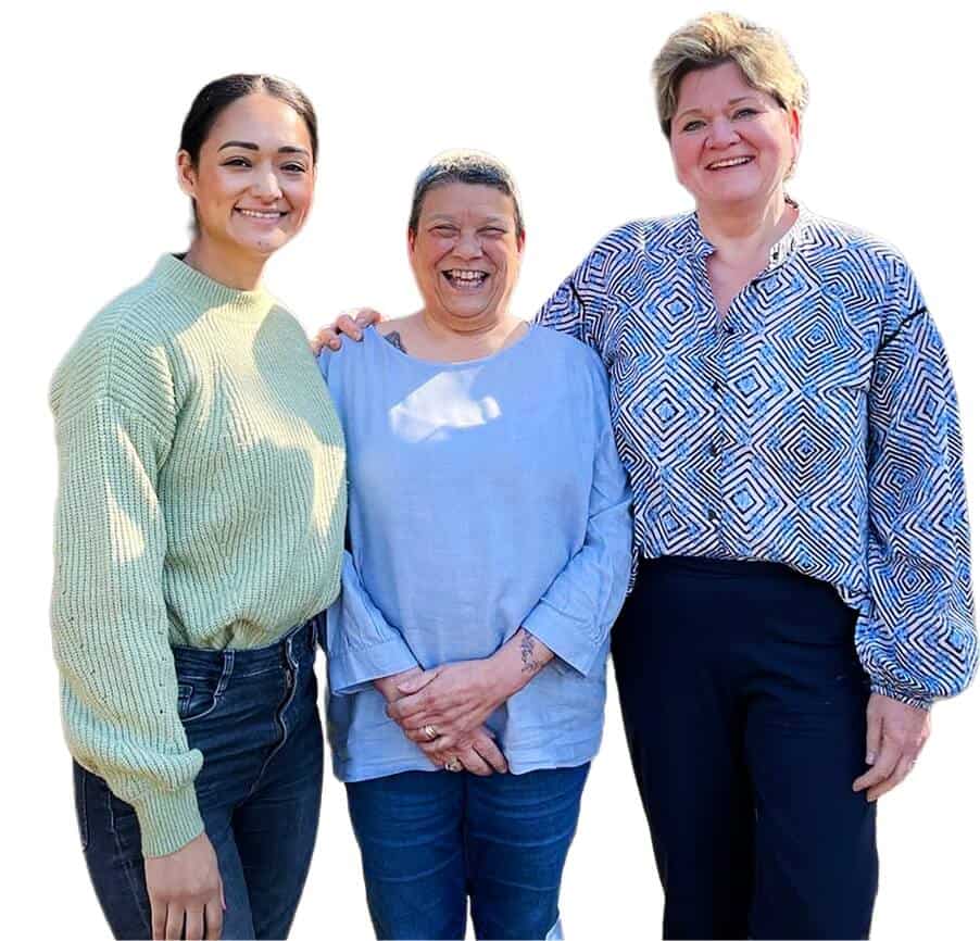 Drie zorgverleners glimlachend, klaar om te ondersteunen bij thuiszorg.