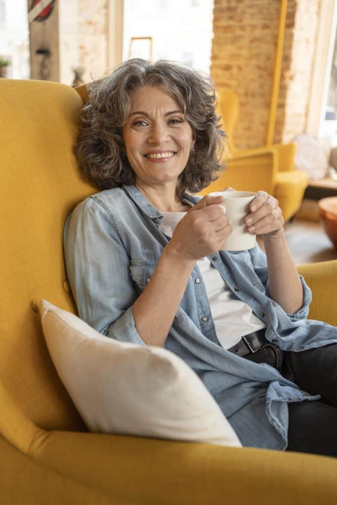 Oudere vrouw geniet van koffie in huiselijke sfeer.