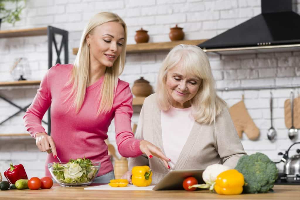 Oudere vrouw krijgt voedingsadvies van verzorgende in keuken.