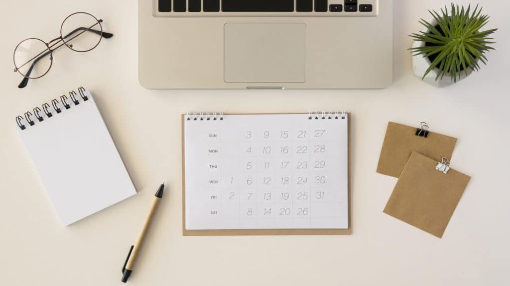 Werkplek met kalender, laptop, notitieboek en planten voor belangrijke dagen.